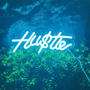 Lifestyle photo showing the ‘Hu$tle’ neon light as part of a modern setup, radiating energy and motivation for entrepreneurs and creators.